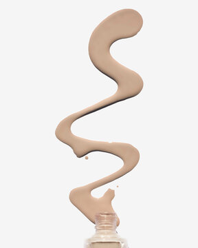 Swirling liquid foundation spilling from an open bottle against a white background.