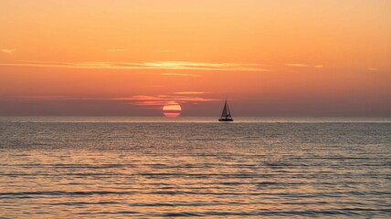 Fototapeta premium Sunset with a distant sailboat on a calm ocean
