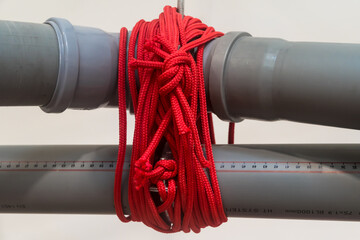 Dettaglio di due tubi grigi di plastica legati da una piccola corda rossa © Andrea Vismara