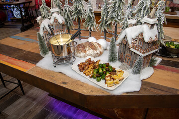 A selection of Christmas food used for a festive fondue including sprouts and pigs in blankets surrounded by festive Christmas decorations on a wooden kitchen table