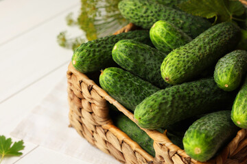 Fresh green cucumbers in wicker box on white table, closeup