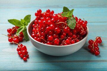 Fresh red currants in bowl and mint on light blue wooden table, closeup