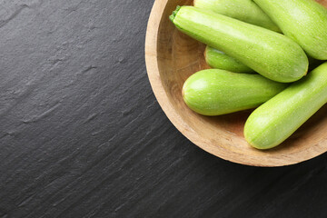 Fresh zucchinis in bowl on dark textured table, top view. Space for text
