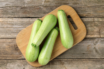Board with fresh zucchinis on wooden table, top view