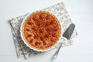 Delicious pecan pie in baking dish and cake server on white wooden table, flat lay