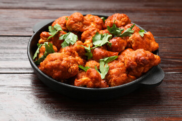 Baked cauliflower buffalo wings with parsley in baking dish on wooden table, closeup