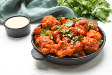 Baked cauliflower buffalo wings in baking dish, parsley and sauce on white marble table, closeup