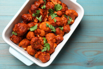Baked cauliflower buffalo wings with parsley in baking dish on light blue wooden table, top view