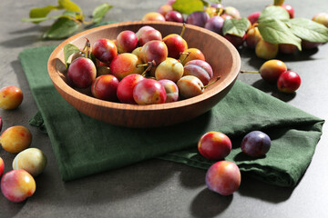 Ripe plums in bowl on grey table