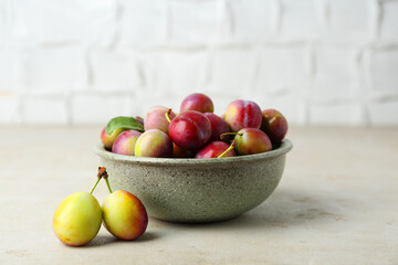 Tasty ripe plums in bowl on grey textured table