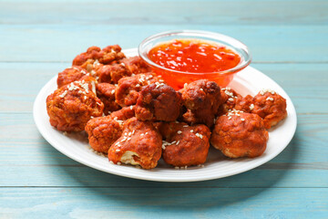 Tasty cauliflower buffalo wings and sauce on light blue wooden table, closeup