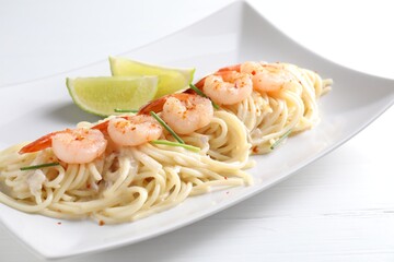 Delicious pasta with shrimps, green onions and lime on white wooden table, closeup