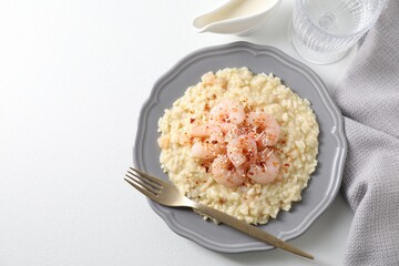 Delicious risotto with shrimps, cheese, sauce and water on white table, top view. Space for text