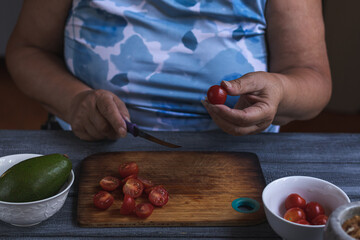 Cropped view of retired woman cutting cherry tomatoes on chopping board.