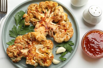 Delicious baked cauliflower steaks with garlic and parsley on white table, flat lay