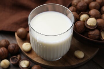 Glass of macadamia milk and nuts on wooden table, closeup