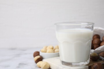 Glass of macadamia milk and nuts on white marble table, closeup. Space for text