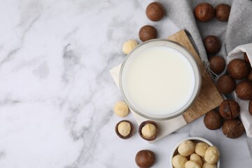 Glass of macadamia milk and nuts on white marble table, flat lay. Space for text