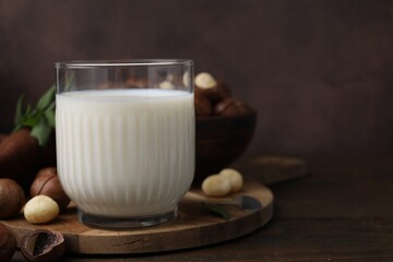 Glass of macadamia milk and nuts on wooden table, space for text