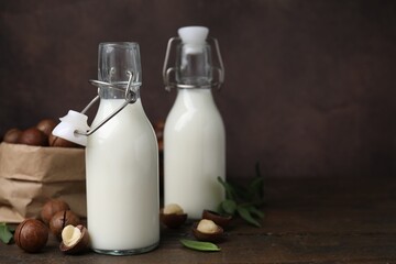 Bottles of macadamia milk and nuts on wooden table. Space for text