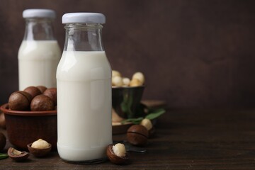 Bottles of macadamia milk and nuts on wooden table. Space for text