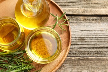 Cooking oil and rosemary on wooden table, top view. Space for text