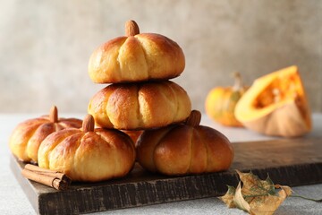Tasty pumpkin shaped buns and cinnamon on light grey table, closeup