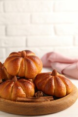 Tasty pumpkin shaped buns and cinnamon sticks on white table