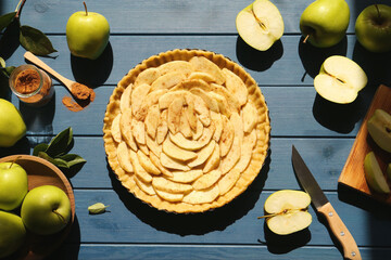 Uncooked homemade apple pie and ingredients on blue wooden table, flat lay