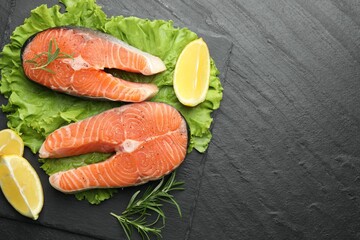 Fresh raw salmon steaks with spices, lemon, lettuce and rosemary on dark textured table, top view. Space for text