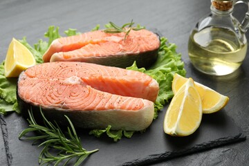 Fresh raw salmon steaks with spices, lemon, lettuce and rosemary on dark textured table, closeup