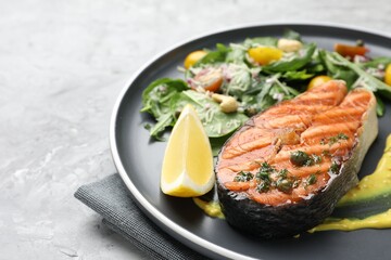 Tasty grilled salmon steak with lemon, sauce and salad on grey textured table, closeup. Space for text