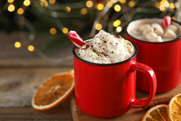 Tasty hot cocoa drink with whipped cream, marshmallows and candy canes in red mugs on table, closeup