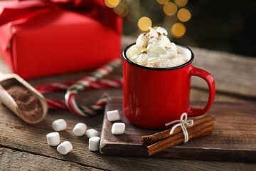 Tasty hot cocoa drink with whipped cream in mug, marshmallows and spices on wooden table