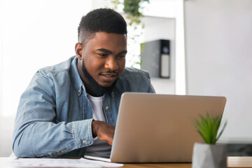 Fototapeta premium Portrait of millennial african american businessman working on laptop in modern office, closeup