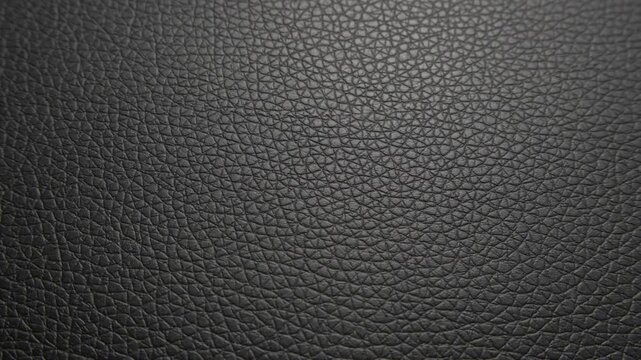 A detailed close-up of black leather, showcasing its natural grain and texture. The surface features fine creases and patterns that emphasize the materials premium quality and durability.