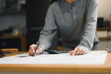 person is engaged in detailed work session, analyzing charts and making notes on large sheet of paper while using calculator. atmosphere conveys focus and productivity.