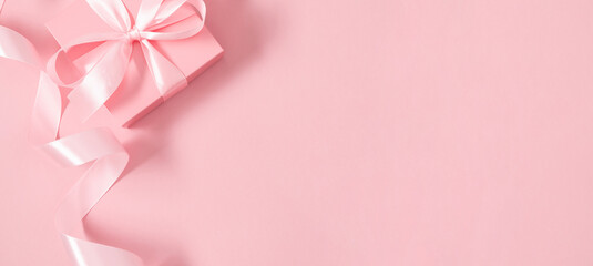 Beautiful pink gift box with satin bow on isolated pastel pink background. Monochrome background....