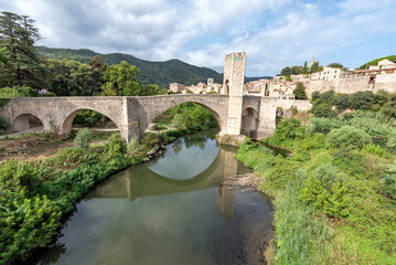 River under a medieval bridge with several arches that give access to a city with a blue sky and white clouds