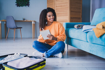 Full body photo of young girl sit floor look empty space packing list suitcase wear orange clothes enjoy modern cozy interior flat indoors
