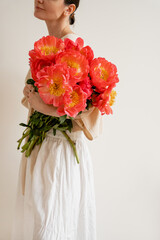 Woman in white skirt and blouse embracing large bouquet of bright red peonies. Minimalist style, elegance