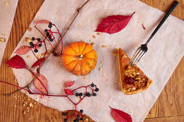 A piece of pumpkin pie lies on a ceramic plate on a wooden table decorated with pumpkins and fall...