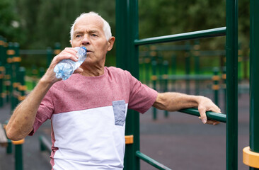 Old man drinking water in outdoor workout station