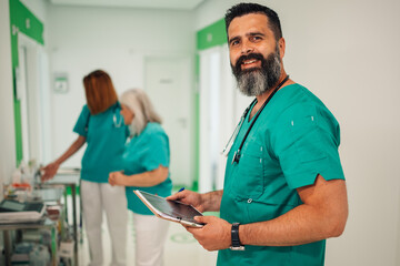 Portrait of a smiling doctor with tablet in hospital corridor with staff.