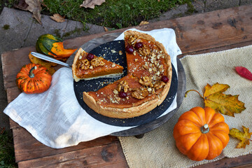 top view of pumpkin pie on a black tray stands on a wooden table with pumpkins and fall leaves