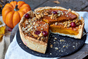 top view of pumpkin pie on a black tray stands on a wooden table with pumpkins and fall leaves