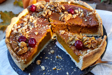 top view of pumpkin pie on a black tray stands on a wooden table with pumpkins and fall leaves