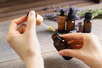 Woman using essential oil at wooden table, closeup