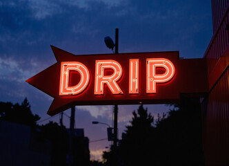 Drip slang word written on a sign outside of a building as neon light sign letters, dark evening in the city