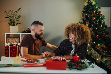 Young couple wrapping christmas presents together at home